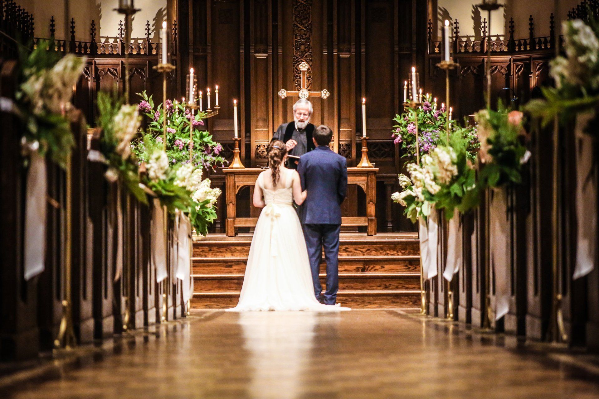 Couple at the altar exchanging vows during a wedding ceremony. Church setting with flowers, candles.
