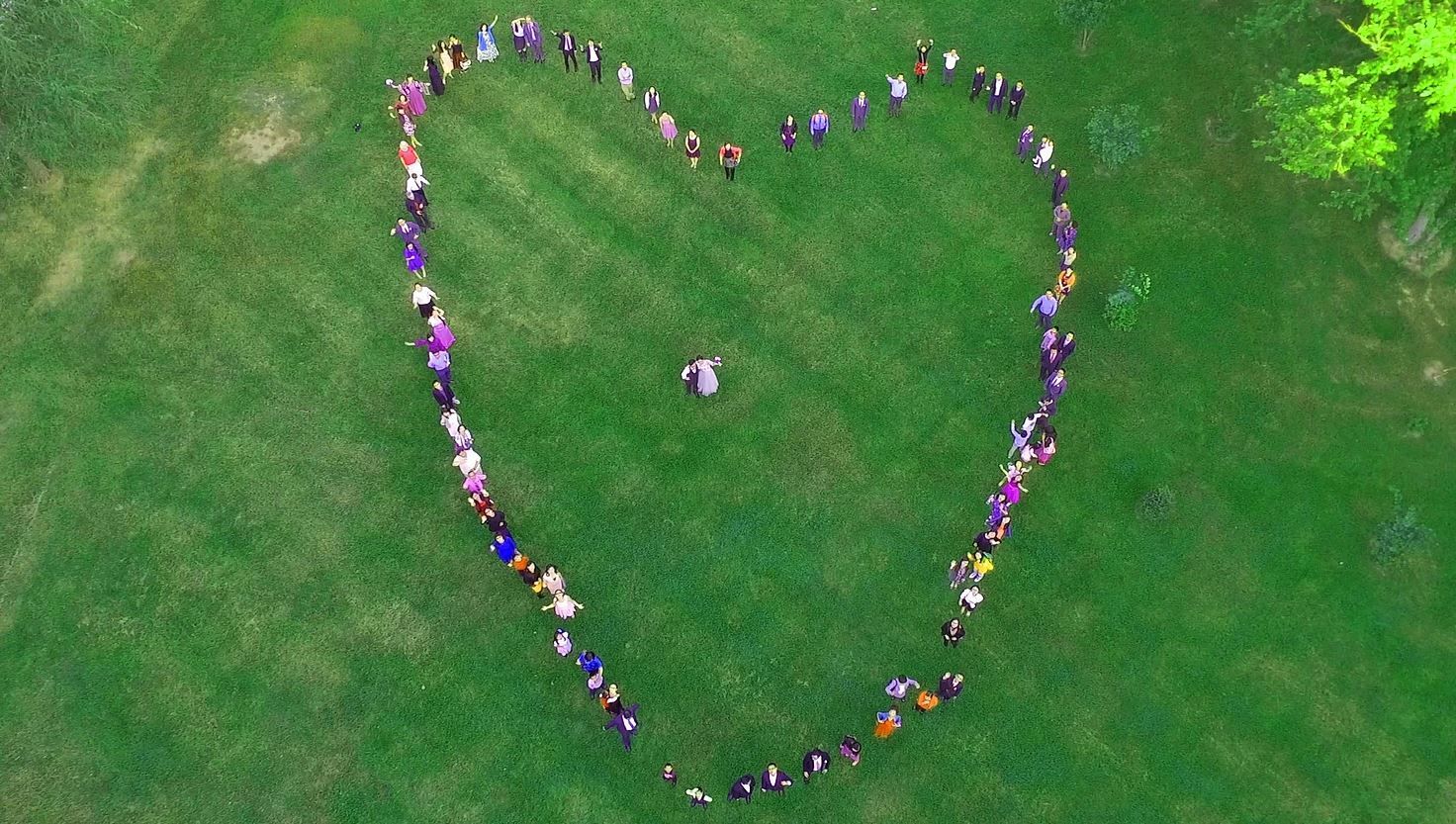 Aerial view of people forming a large heart shape on a green grassy field.
