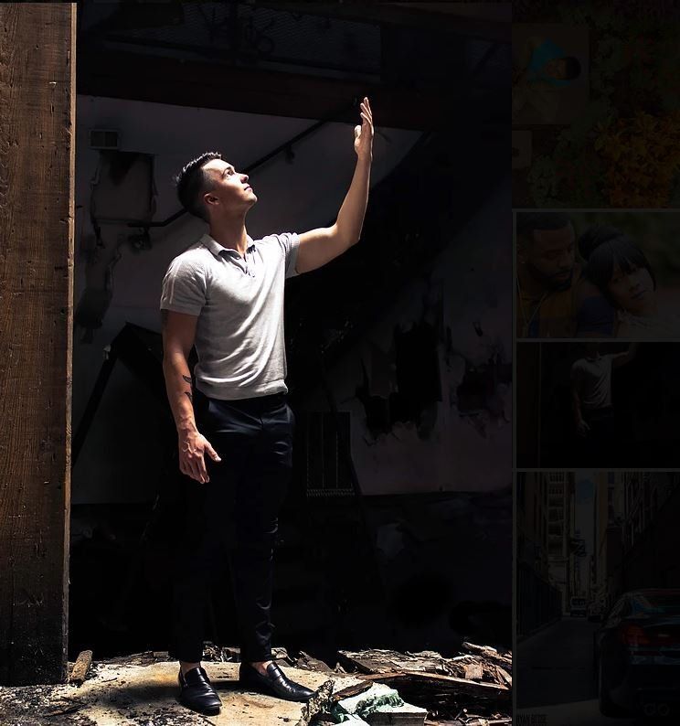 Man in a gray polo shirt and black pants raises his arm towards the ceiling in a dark, dilapidated room.
