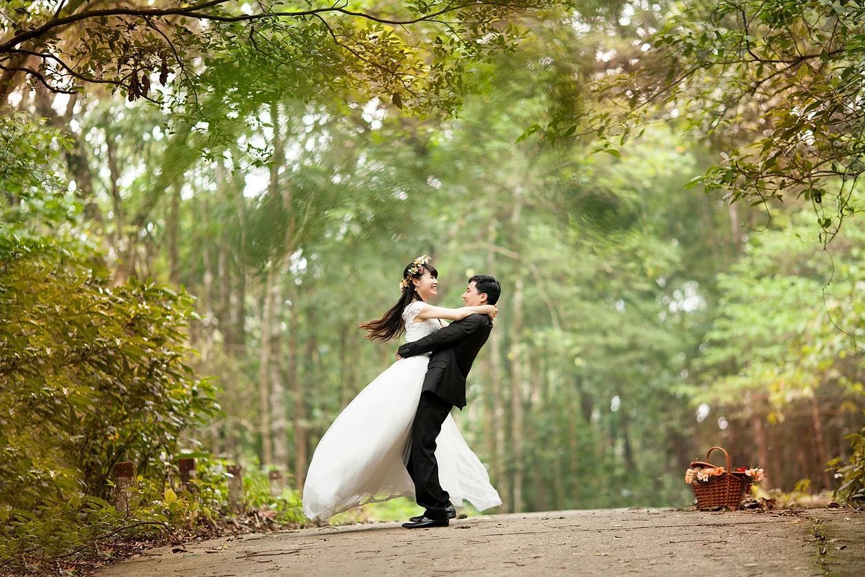 Couple embraces, bride in white dress, groom in black suit, on a path in a forest, joyous.