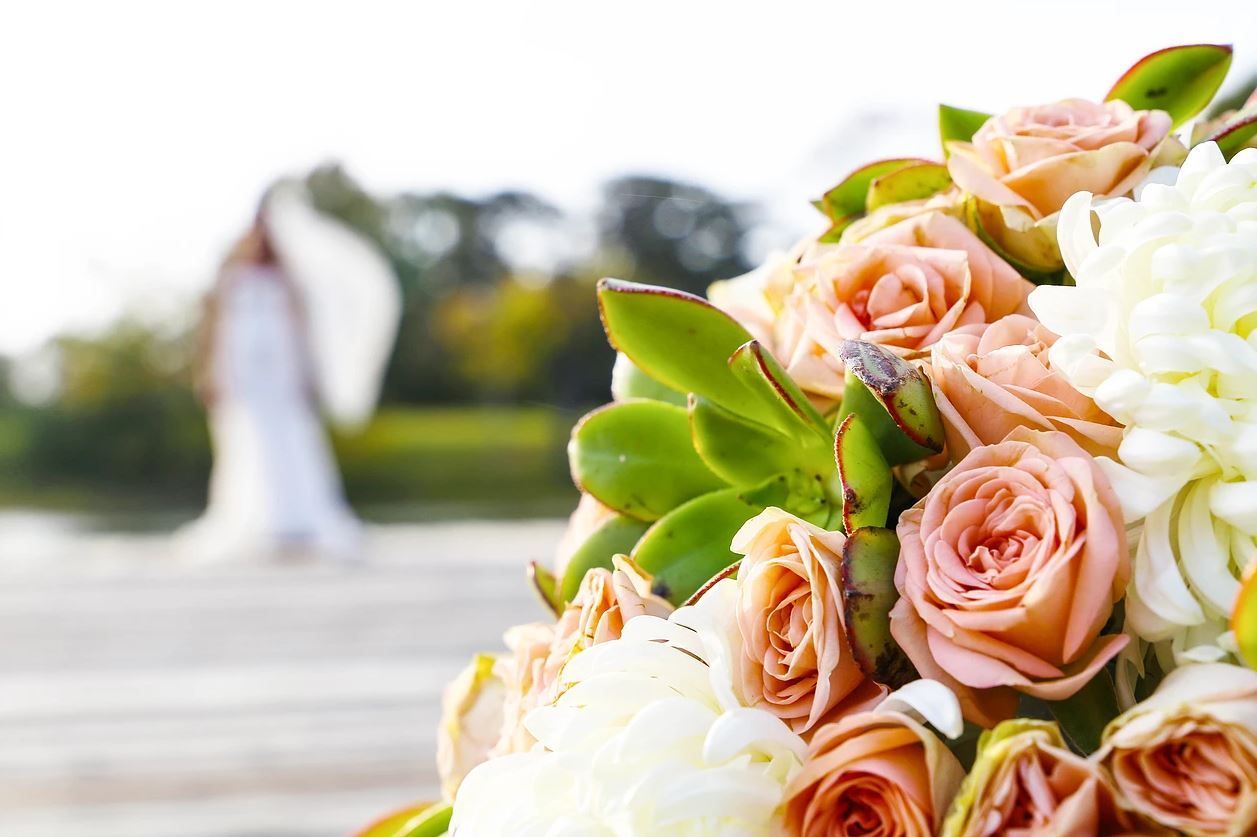 Wedding bouquet of peach roses and white flowers, bride in background, blurred.