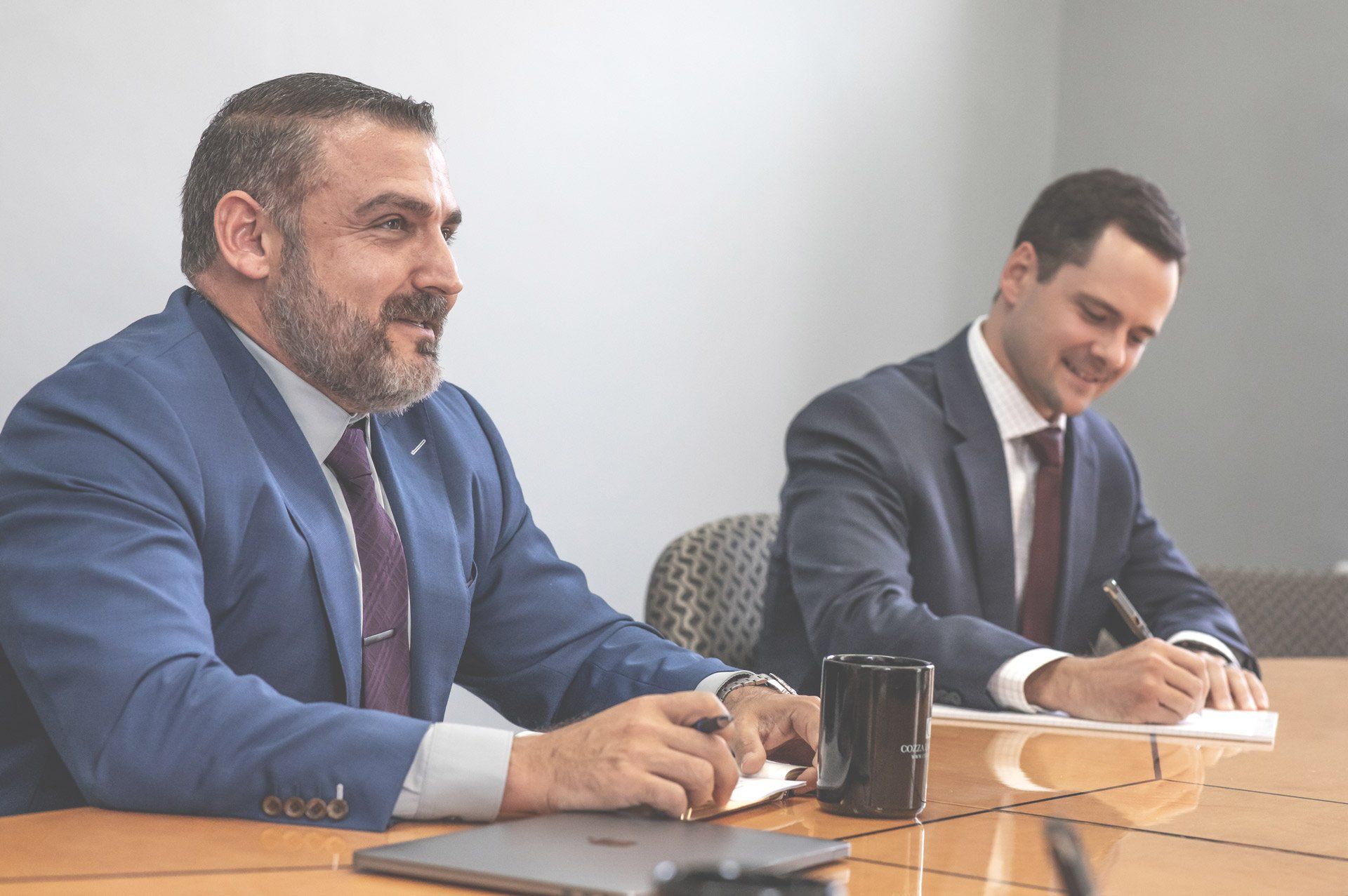 Two men in suits and ties are sitting at a table.
