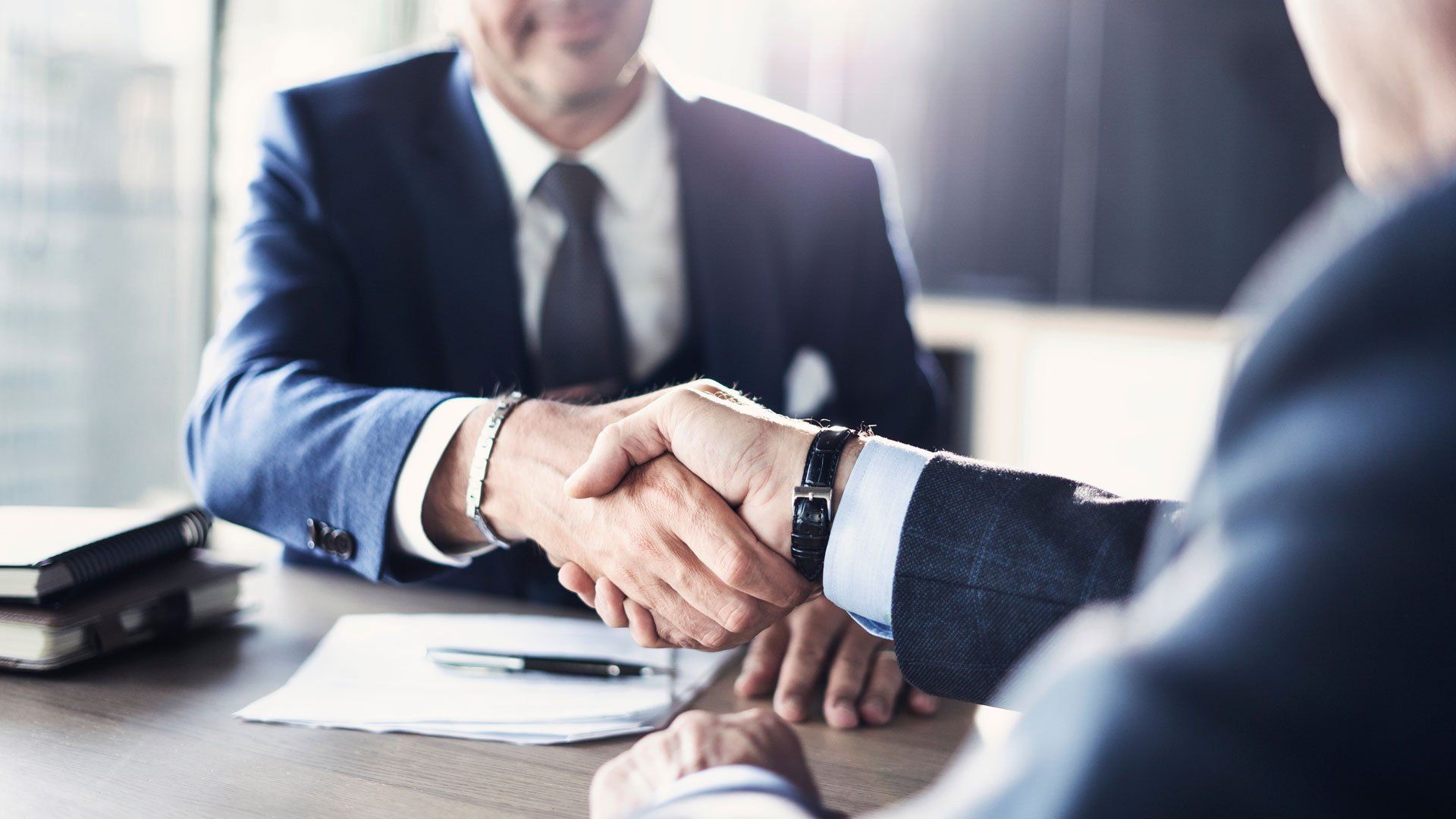 Two businessmen are shaking hands while sitting at a table.
