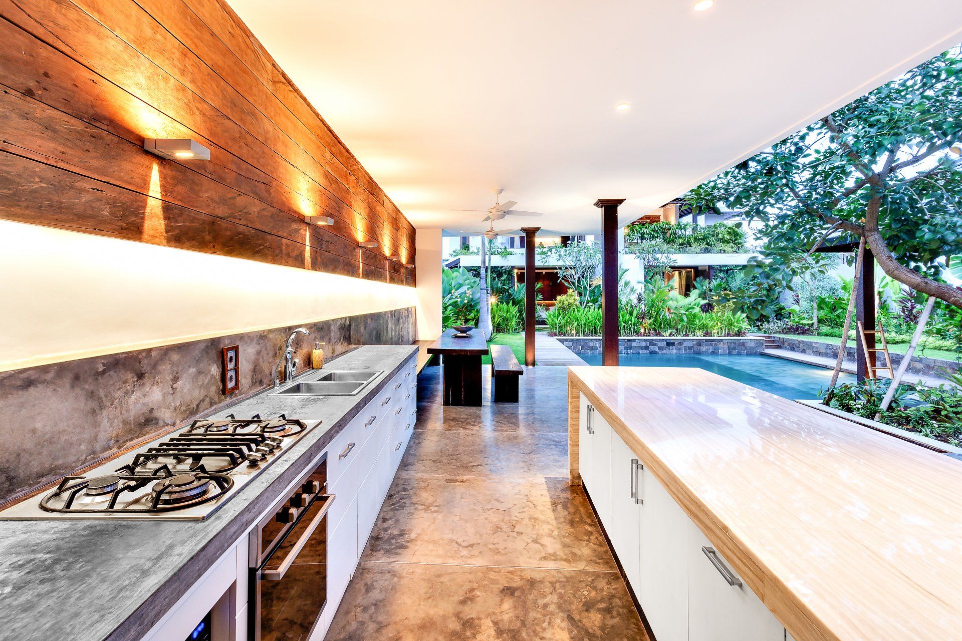 Outdoor kitchen with a stove an countertop next to garden including a pool in luxury hotel or house