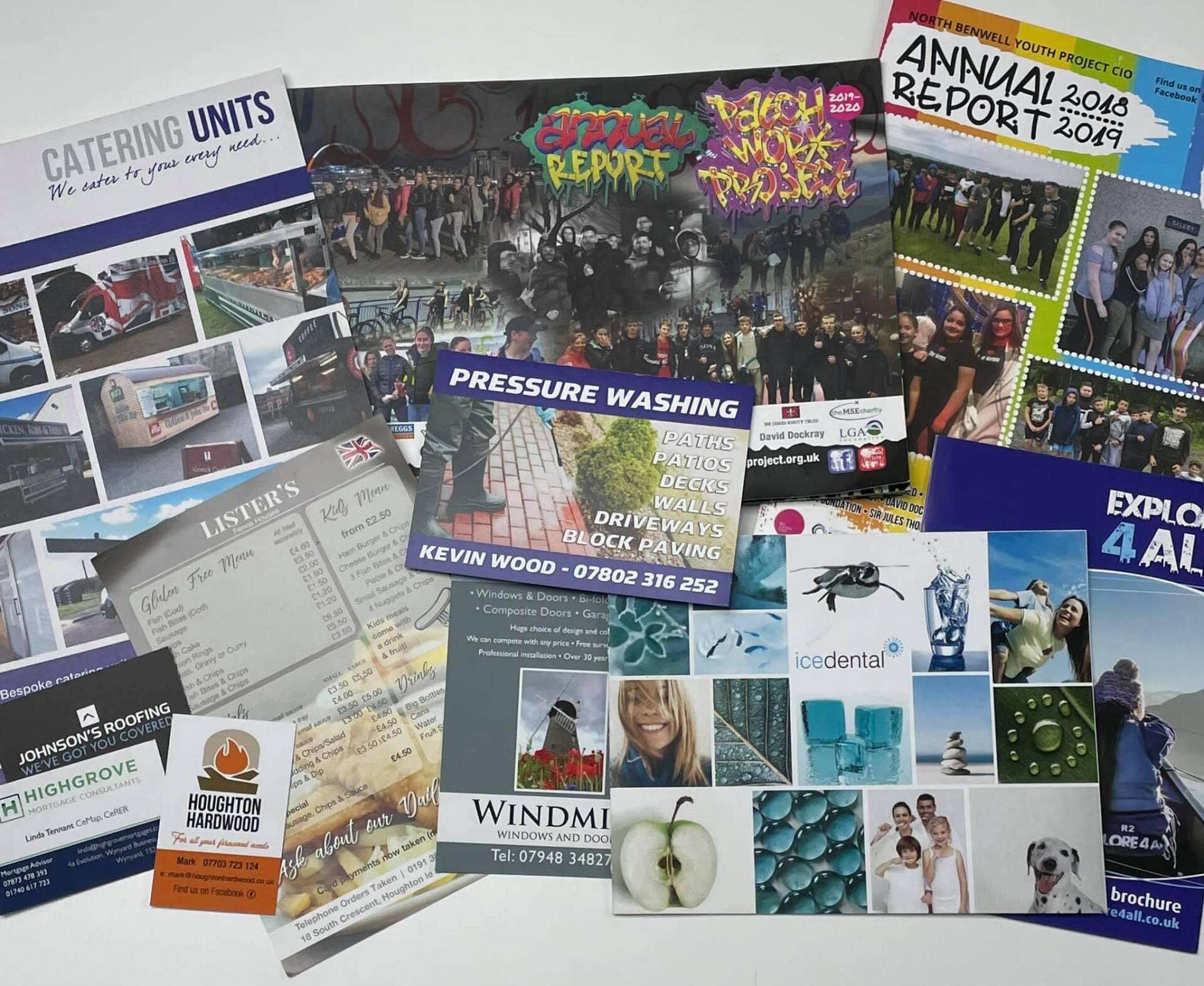 Pile of colorful printed documents, including reports, brochures, and flyers, with photos and text.