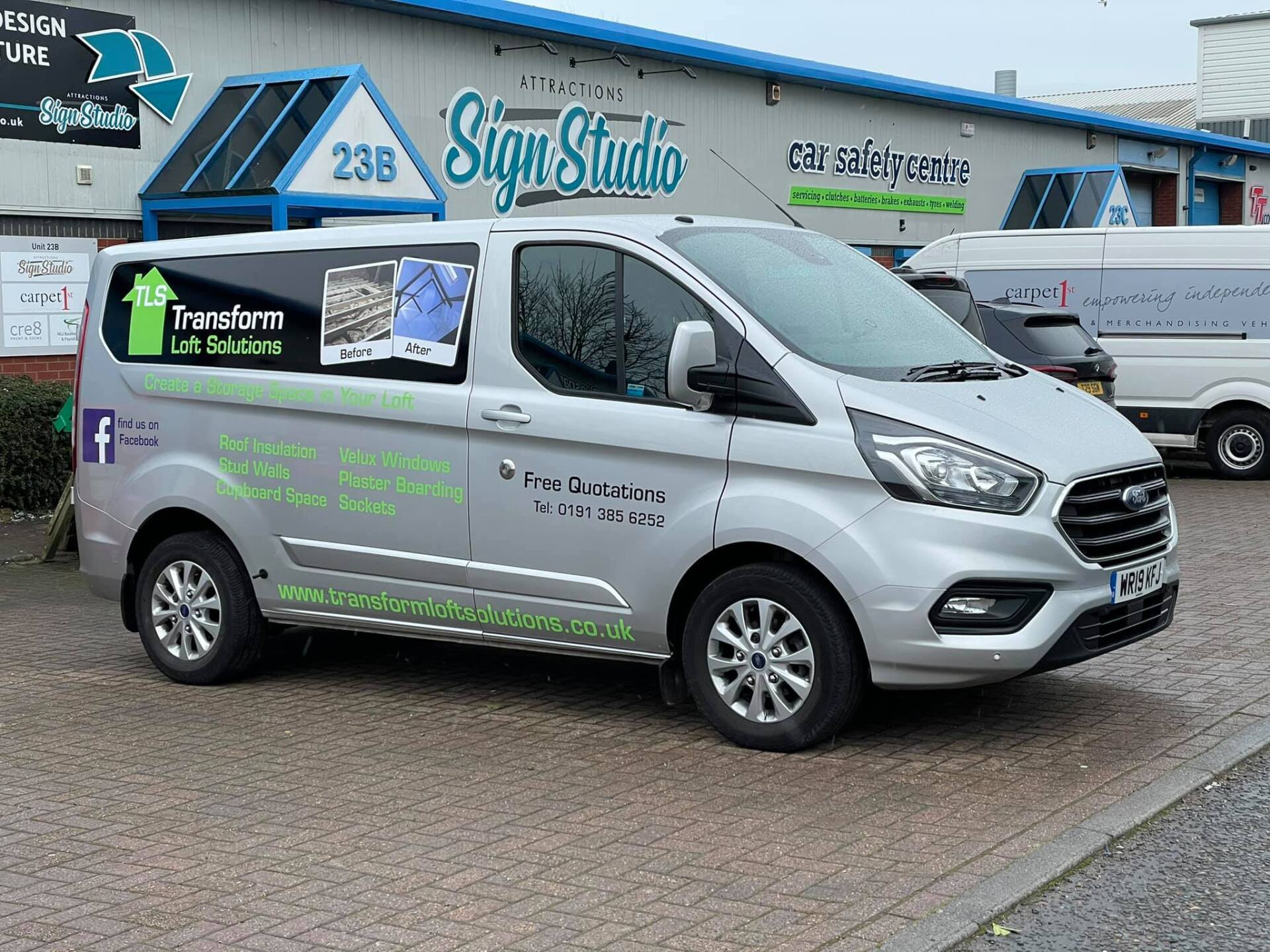 Silver van with business graphics parked in front of a sign studio.