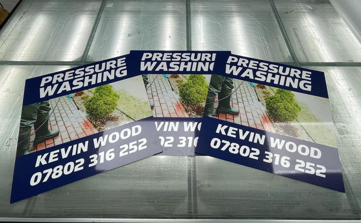 Three pressure washing signs with contact information. Blue and white text on a shiny surface.