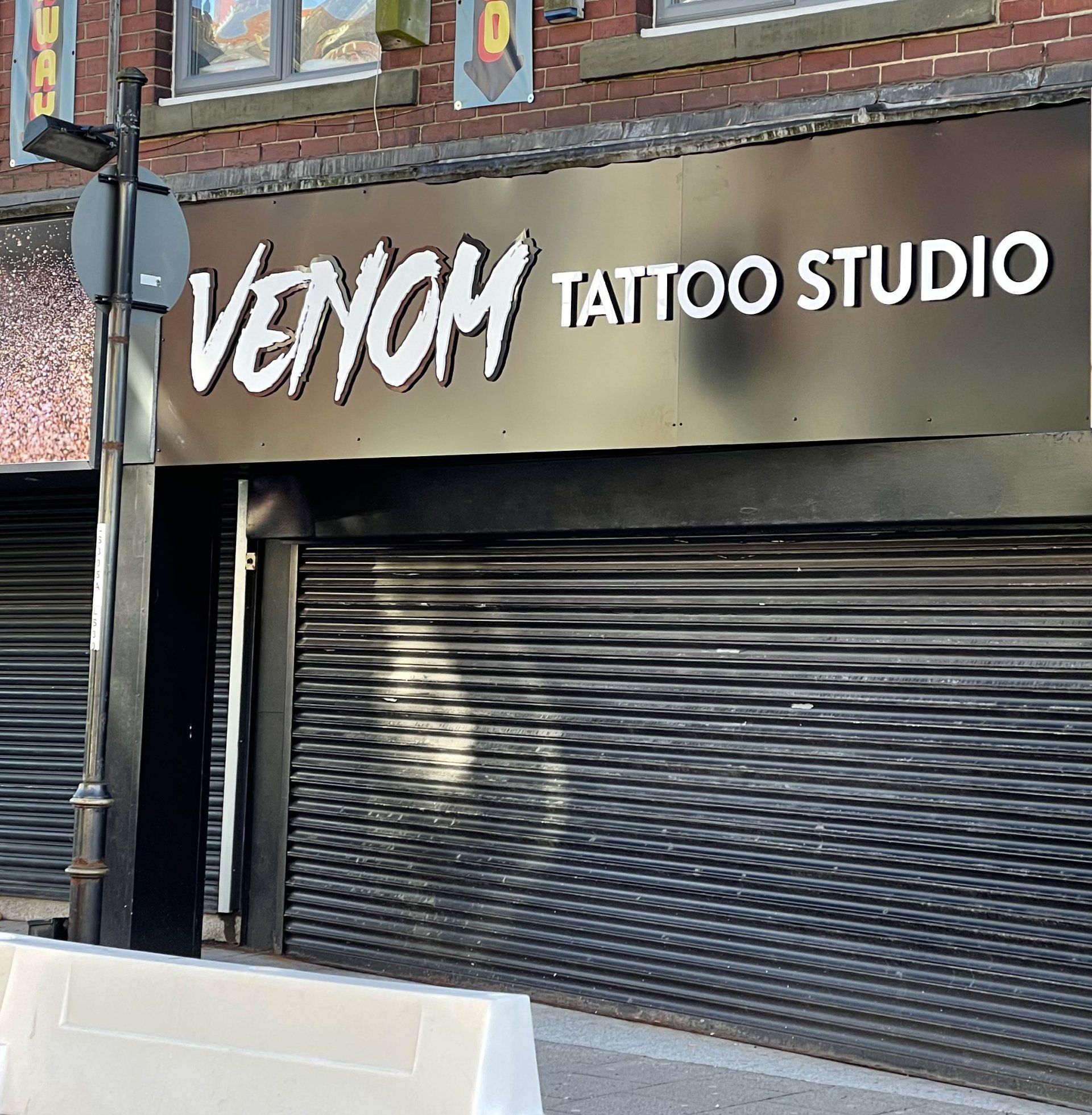 Venom Tattoo Studio storefront with black sign, white lettering, and closed metal shutters.