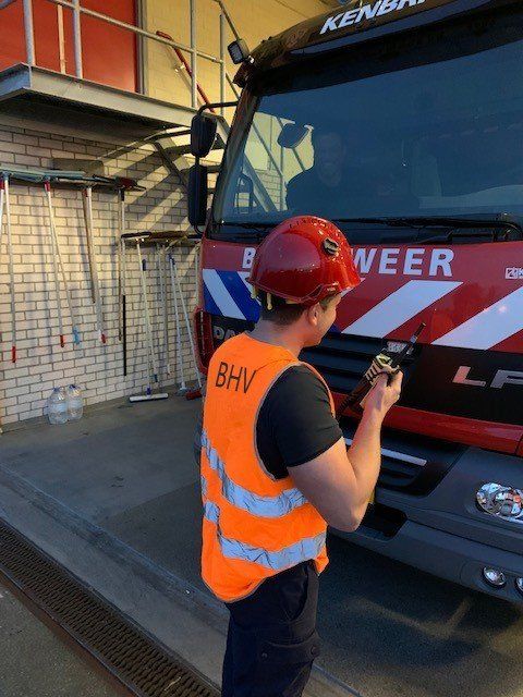 Een medewerker in een oranje veiligheidsvest gebruikt een handheld apparaat naast een rode KLM-bus op een depot.