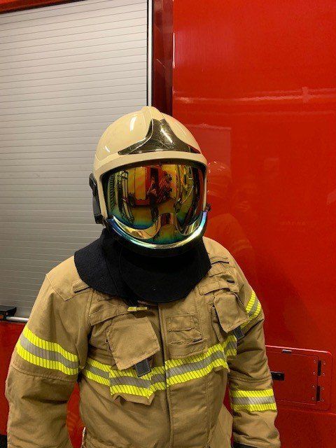 Een brandweerman in beige brandweerpak en met een reflecterend vizier op zijn helm 