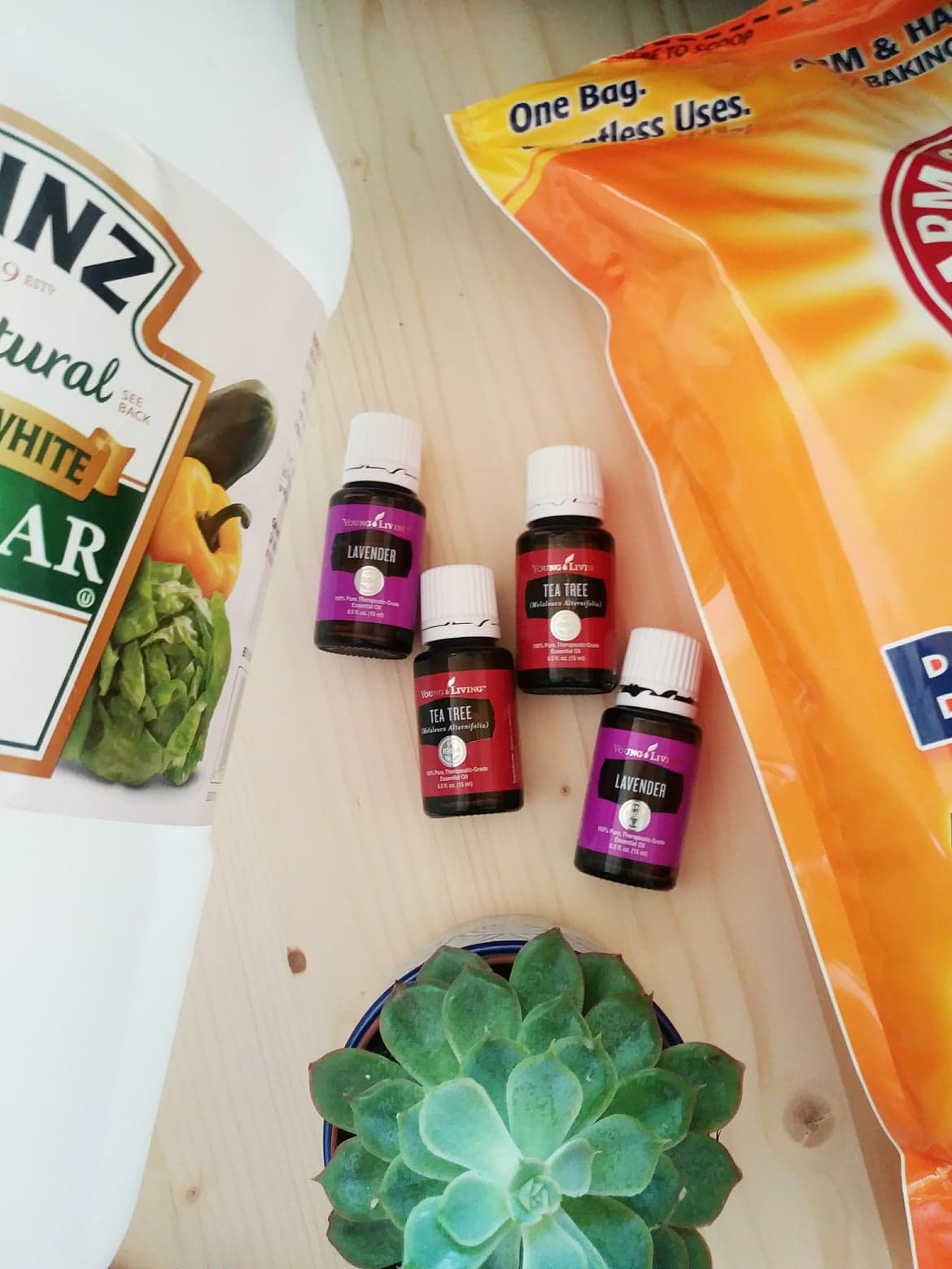 Essential oils, a succulent, and a bag of greens on a light wooden surface.