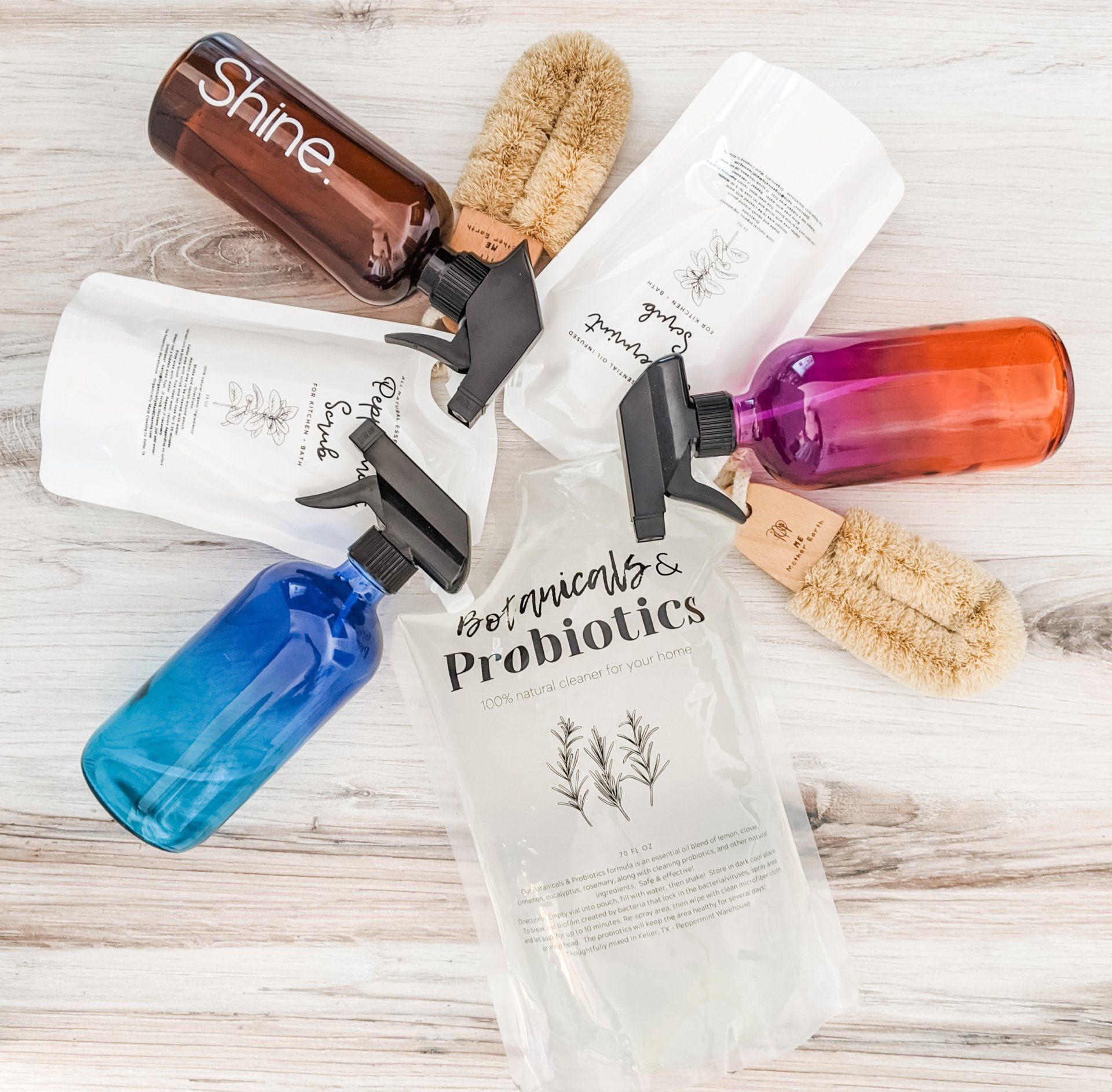 Assorted shampoo, conditioner, and probiotic bottles with brushes on a light wood background