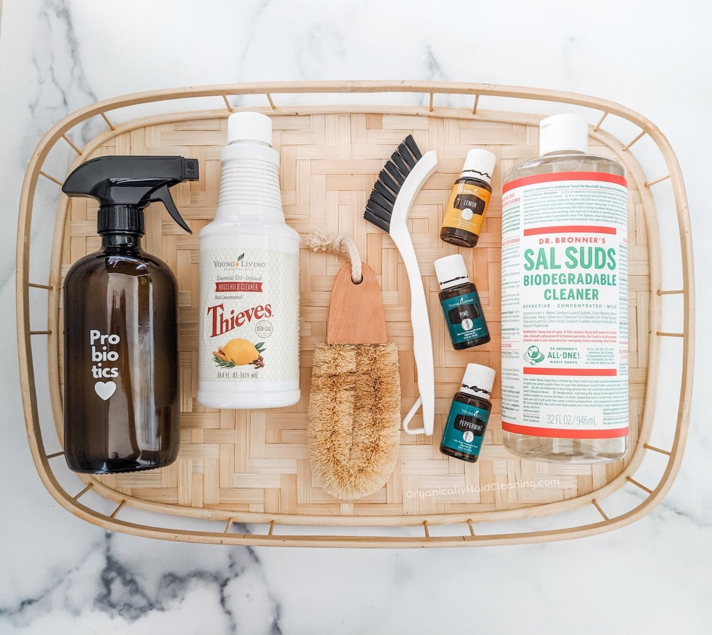 Cleaning supplies in a wicker tray on a marble surface, including spray bottles, brushes, and detergent bottles