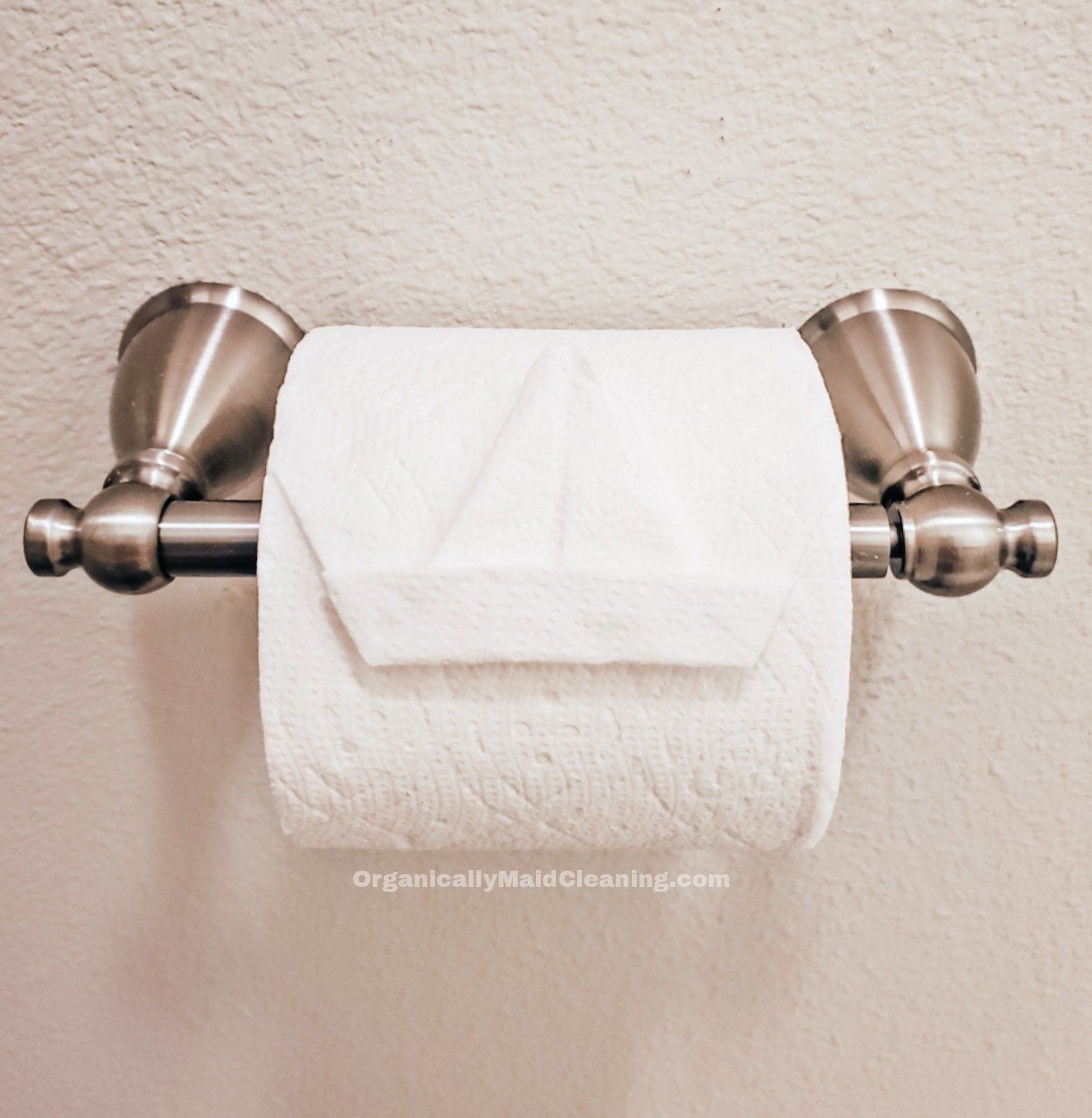 A roll of toilet paper hanging on a metallic holder with the end folded into the shape of a small sailboat.