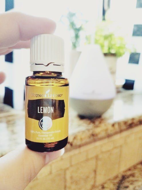 Hand holding a small lemon essential oil bottle in front of a blurred indoor background