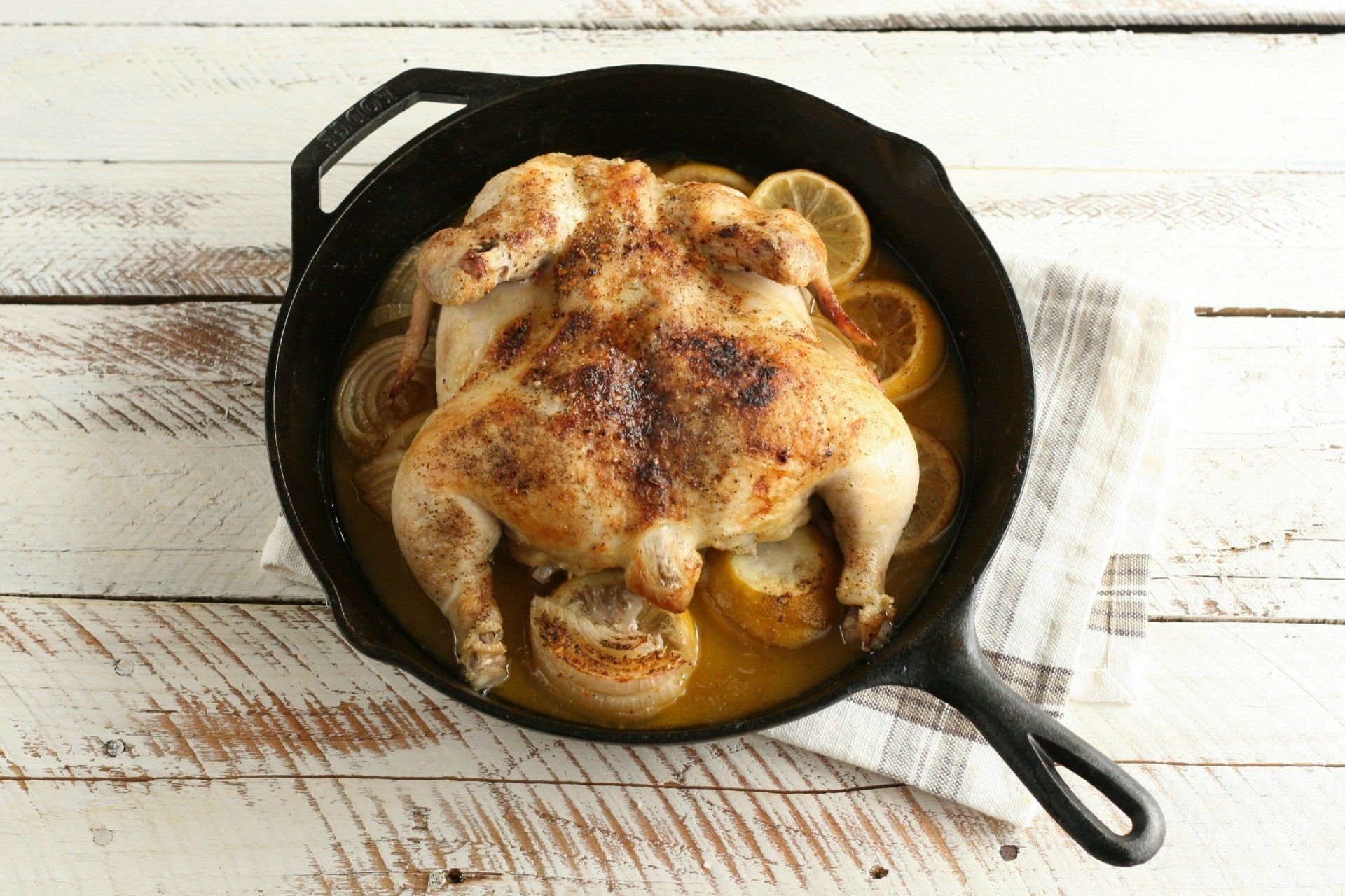 Roasted chicken in a cast-iron skillet with potatoes on a rustic white wooden table