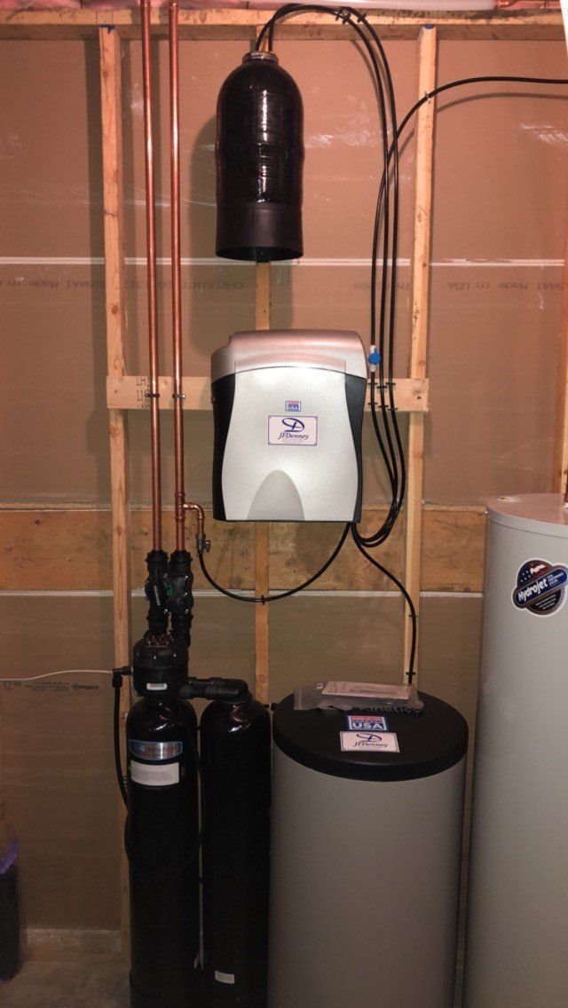 A water softener is installed in a basement next to a water heater.