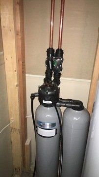 A water filter is sitting in a room next to a copper pipe.