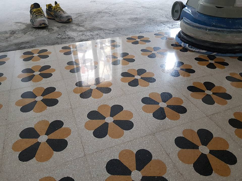 Floral tiled floor being polished with a machine, safety shoes in the background.