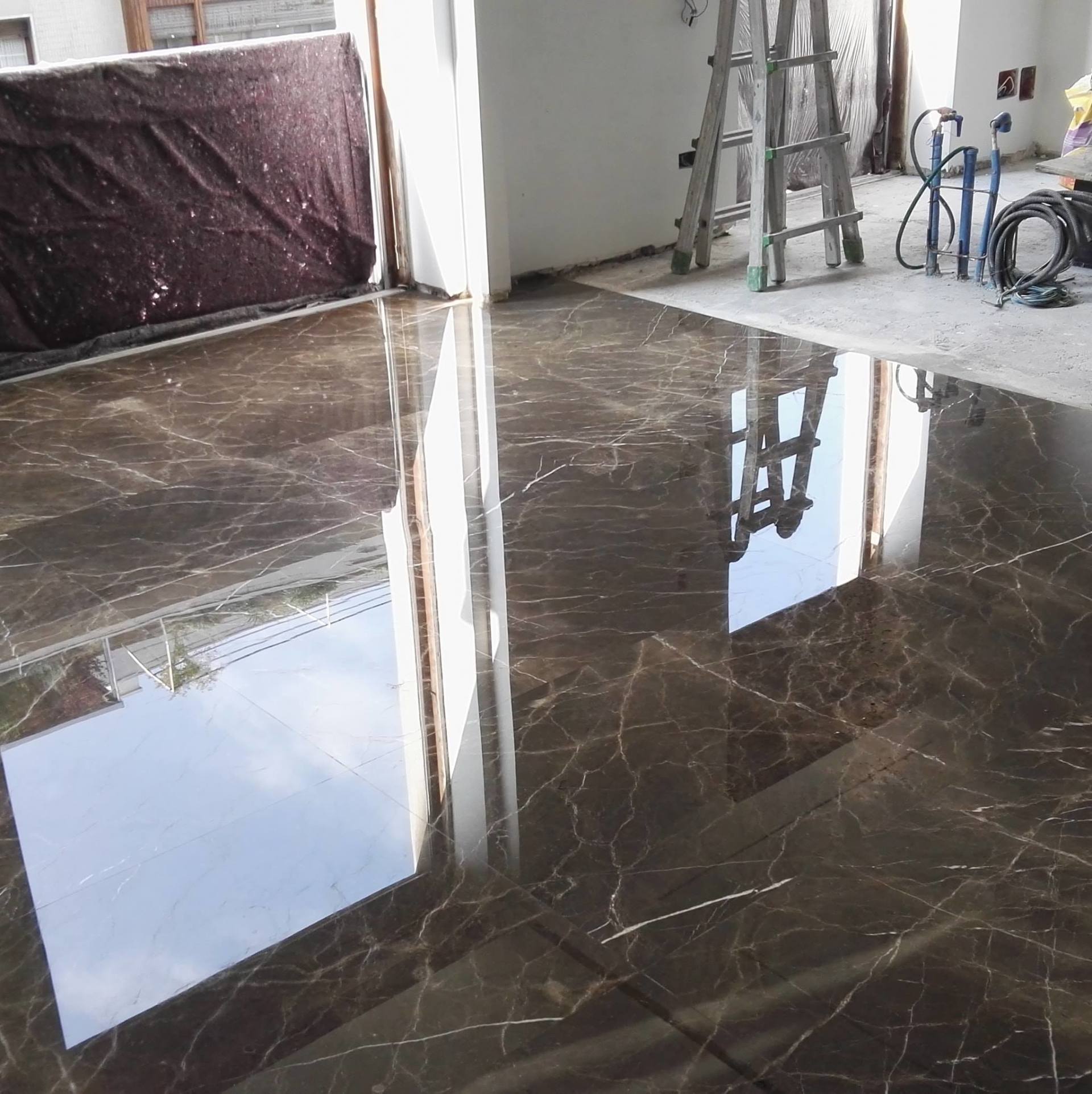 Polished dark brown marble floor reflects light and a ladder, under construction.