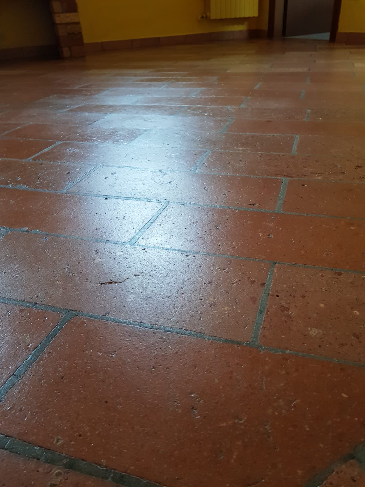 Red tile floor with dark grout, reflecting light in a room with yellow walls.
