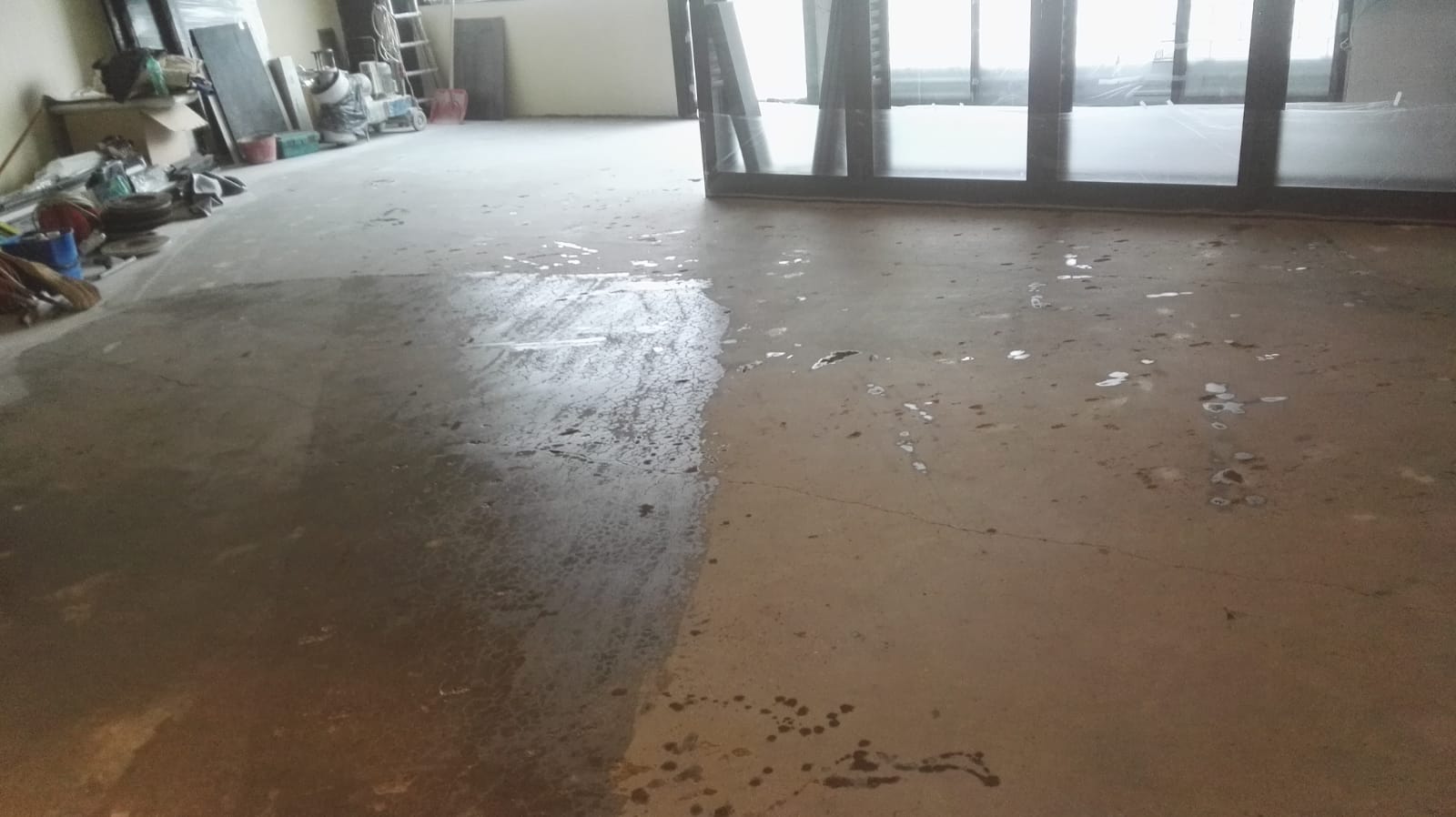 Concrete floor in a room, partially covered with a wet, grey substance. Debris scattered across.