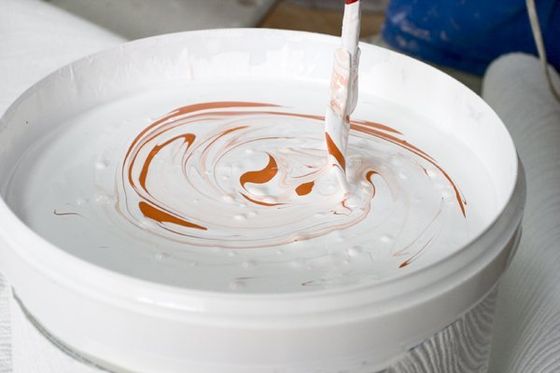 secchio in cui si stanno mescolando vernici di colori bianco e arancione