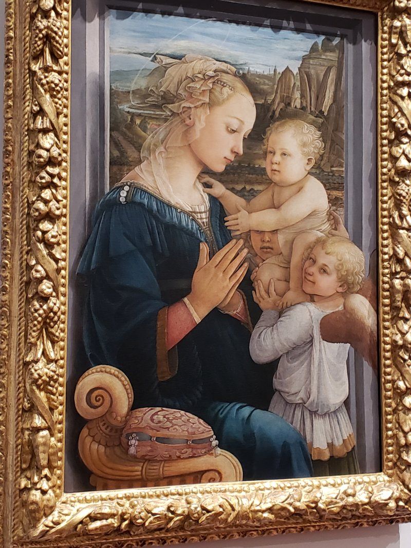 A painting of a woman holding three children in a gold frame.