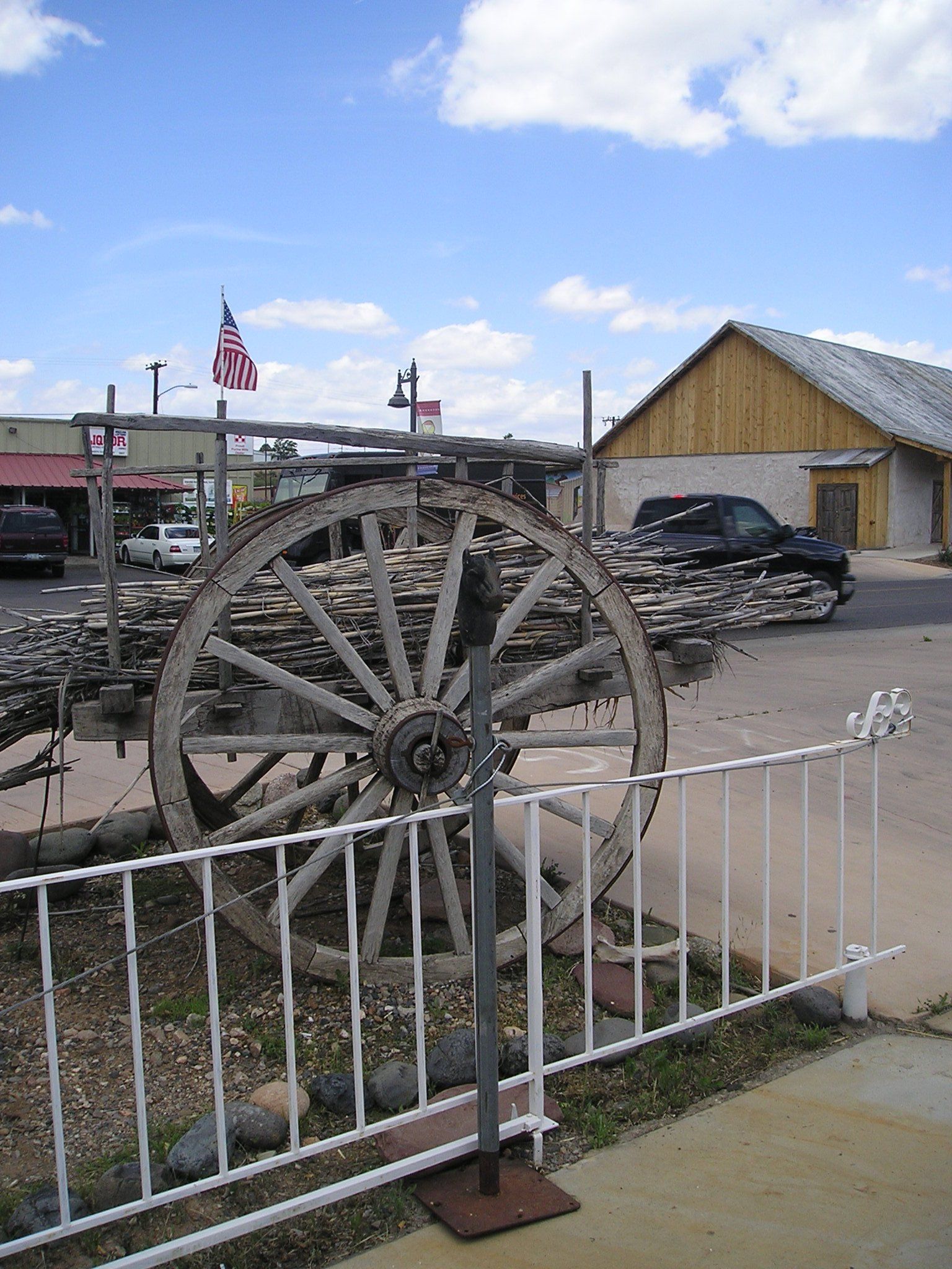 A large wooden wheel is behind a fence in front of a building