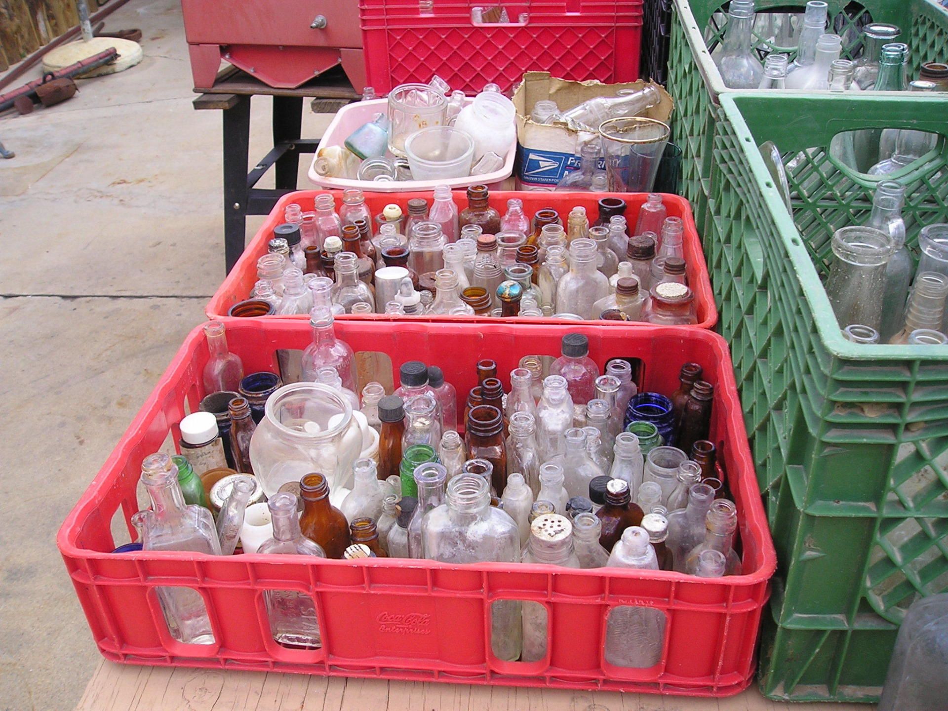 A red crate filled with empty bottles sits next to a green crate