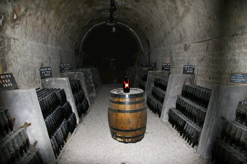 A bottle of wine is sitting on top of a wooden barrel in a wine cellar.