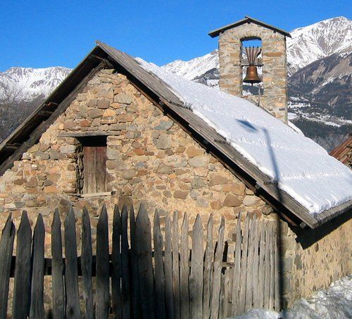 A stone building with snow on the roof and mountains in the background