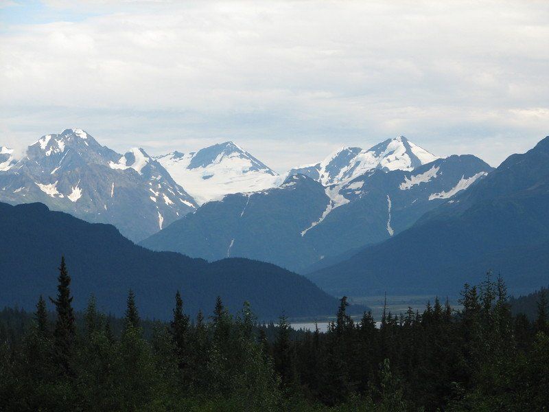 A mountain range with trees in the foreground and a lake in the background