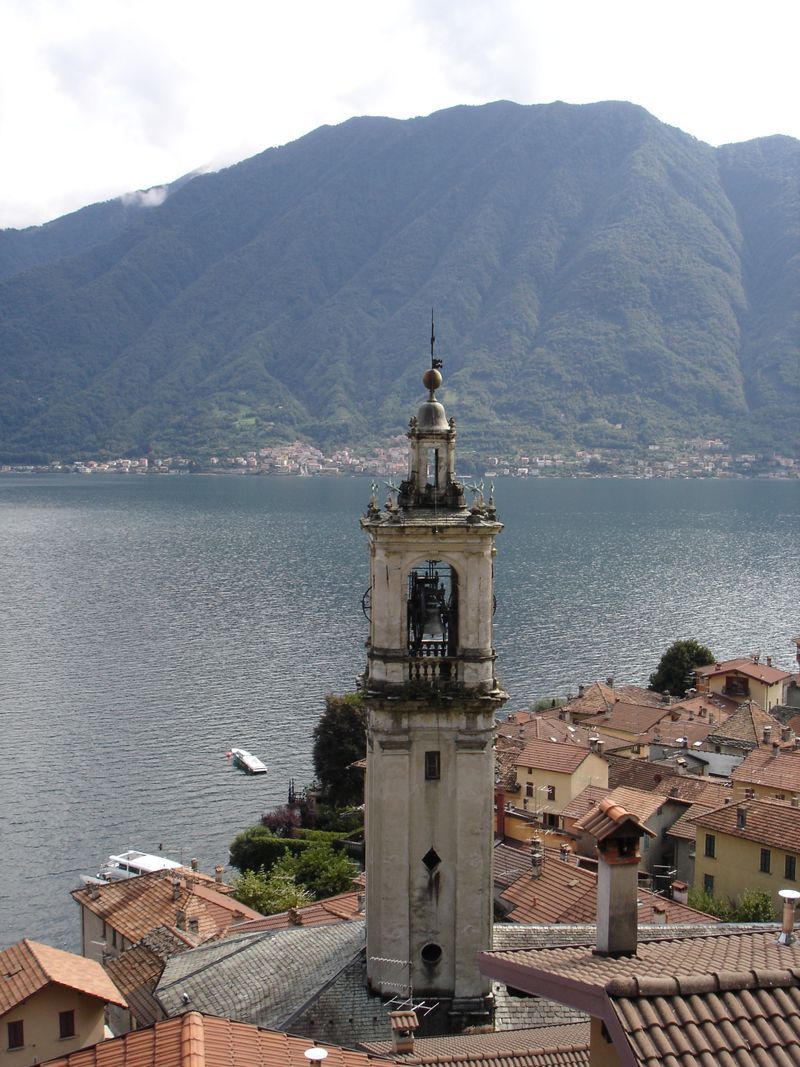 A bell tower with mountains in the background and a lake in the foreground