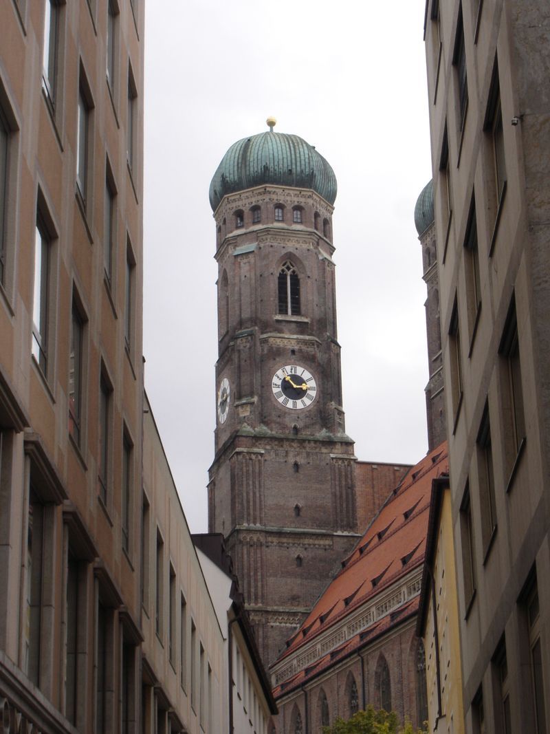 A clock tower with a green dome is between two buildings