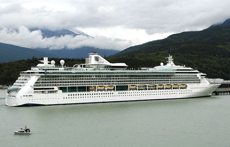 A large cruise ship is docked in the water with mountains in the background