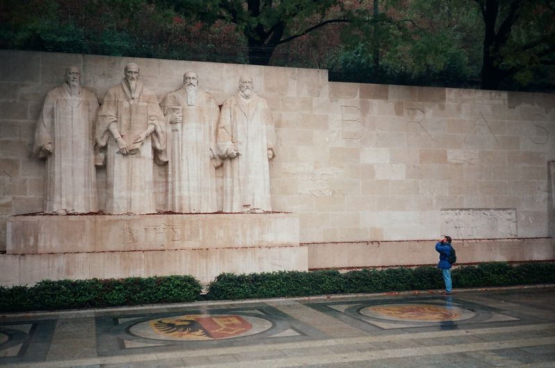 A man is standing in front of a statue of a group of people.