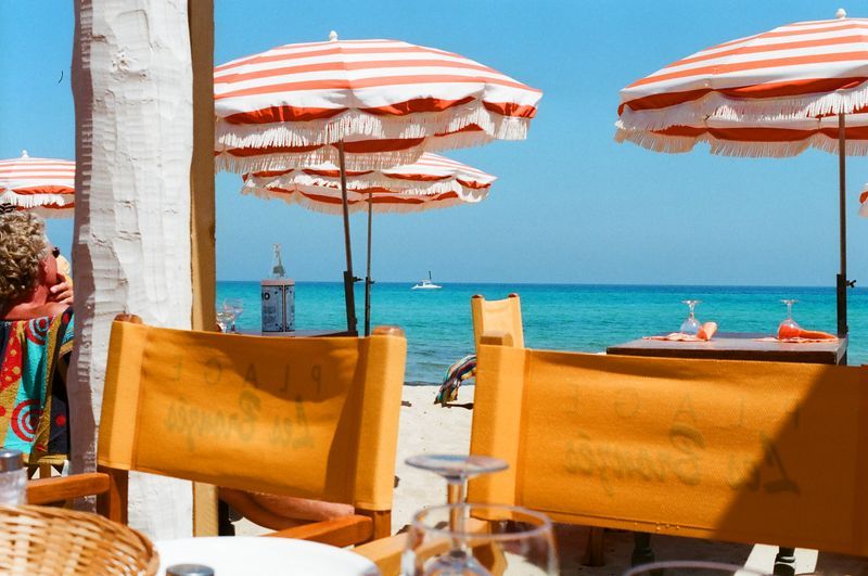 A woman is sitting at a table on the beach under umbrellas.