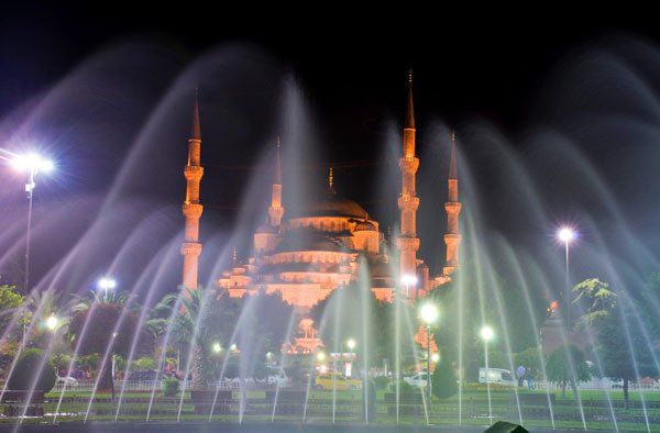 A fountain in front of a mosque at night