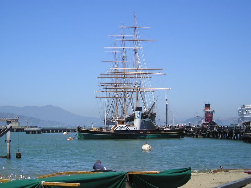 A large sailboat is docked in a harbor with mountains in the background