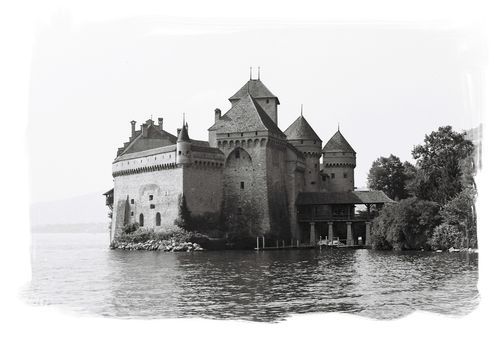 A black and white photo of a castle on a small island in the middle of a lake.