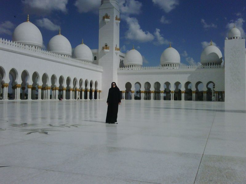 A woman in a black dress stands in front of a large white building