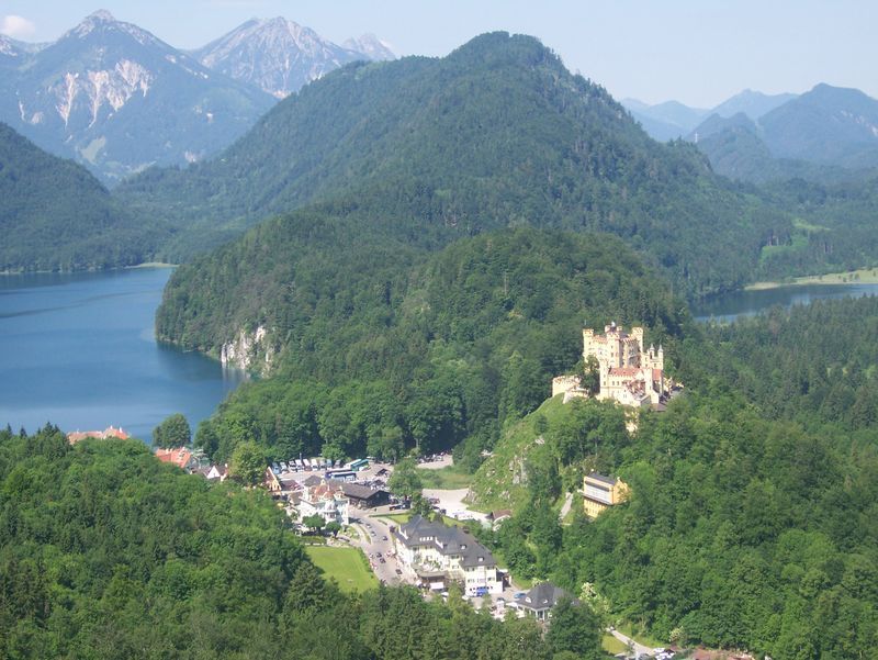 A castle sits on top of a hill overlooking a lake surrounded by mountains.
