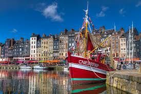 A red boat is docked in a harbor in front of a city.