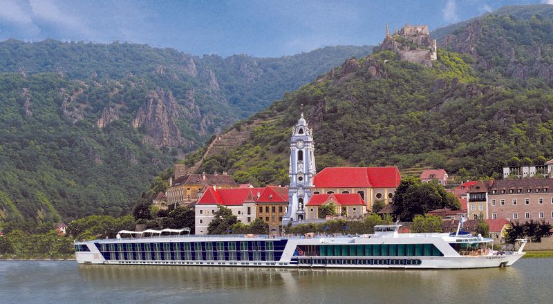 A cruise ship is floating on a river in front of a small town.