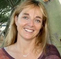 A woman is smiling for the camera while standing in front of a tree.