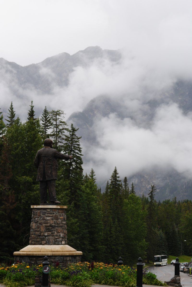 A statue of a man stands in front of a foggy mountain
