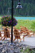 A row of wooden chairs sitting next to a lamp post with flowers hanging from it.