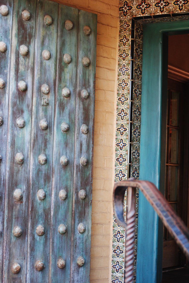 A blue door with a wrought iron railing is next to a brick wall.