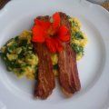 A white plate topped with bacon , eggs and a flower.